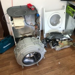 Paweł Roliński ROL-FIX - Rozłożona pralka z widocznymi częściami, narzędzie Makita obok. Elementy pralki na podłodze, ukazujące etap demontażu lub naprawy urządzenia.