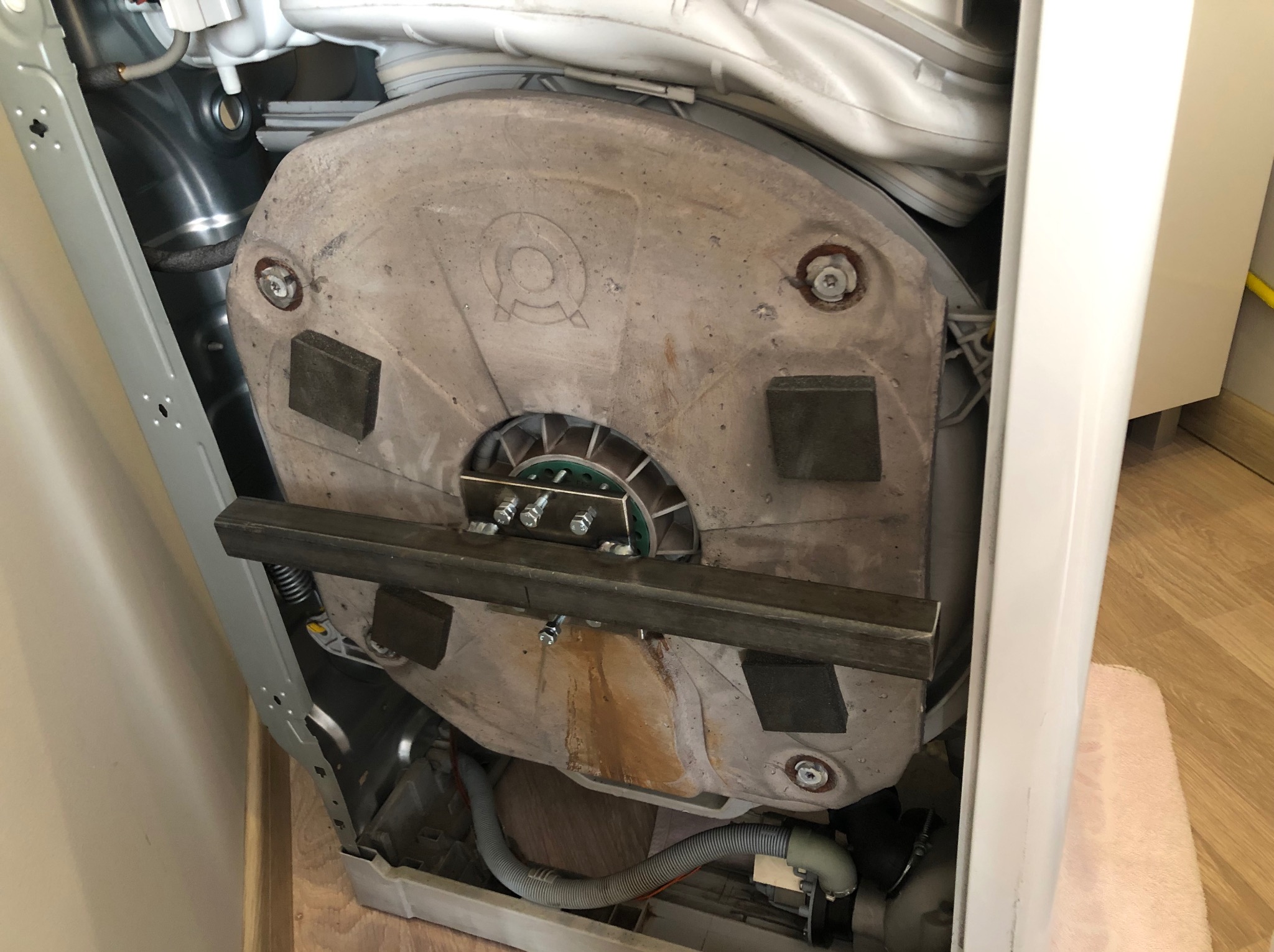 Wnętrze pralki automatycznej w Łodzi. Widoczny betonowy obciążnik bębna z zamocowanymi elementami metalowymi i śladami użytkowania.