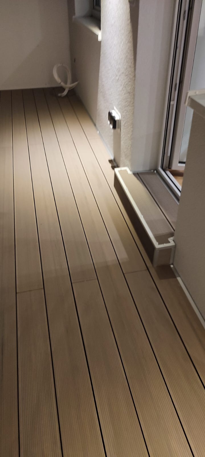 Nowoczesny balkon z desek kompozytowych w odcieniach beżu, widoczne łączenia desek i próg drzwi balkonowych.