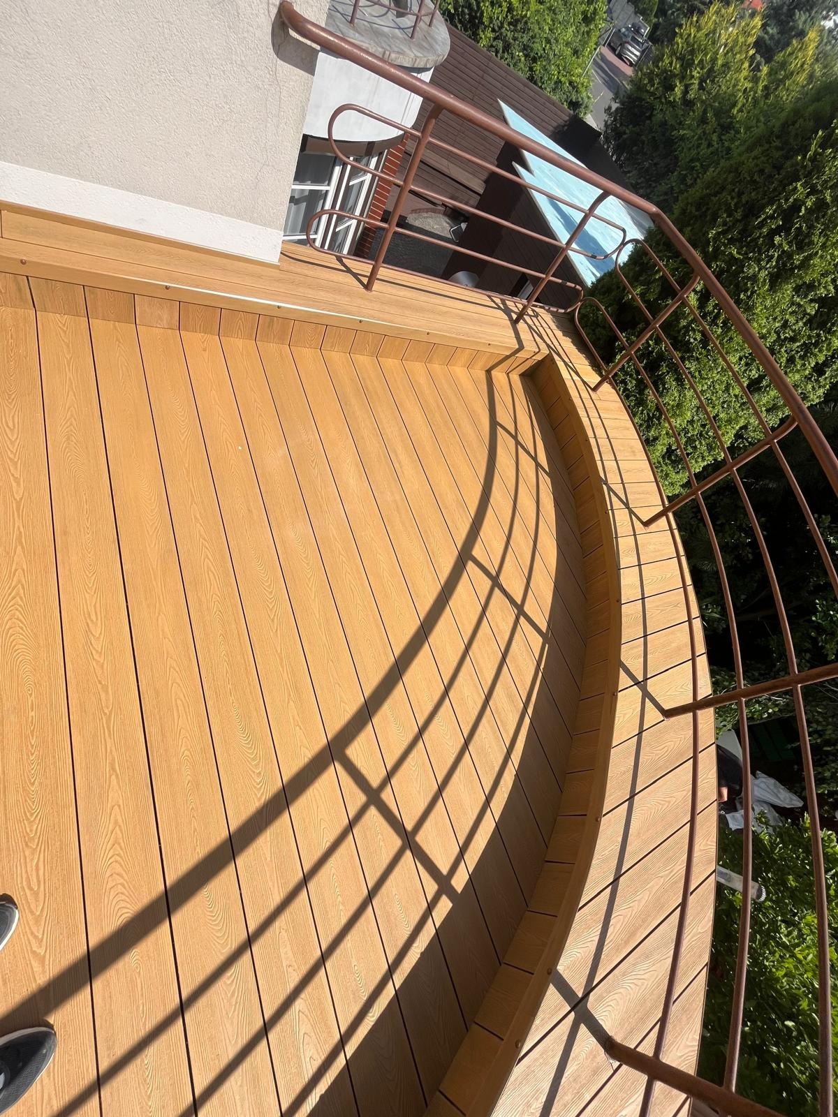 Wykończony balkon z deską kompozytową i metalową balustradą w Krakowie. Widok z góry, ukazujący detale wykończenia i cień rzucany przez balustradę.