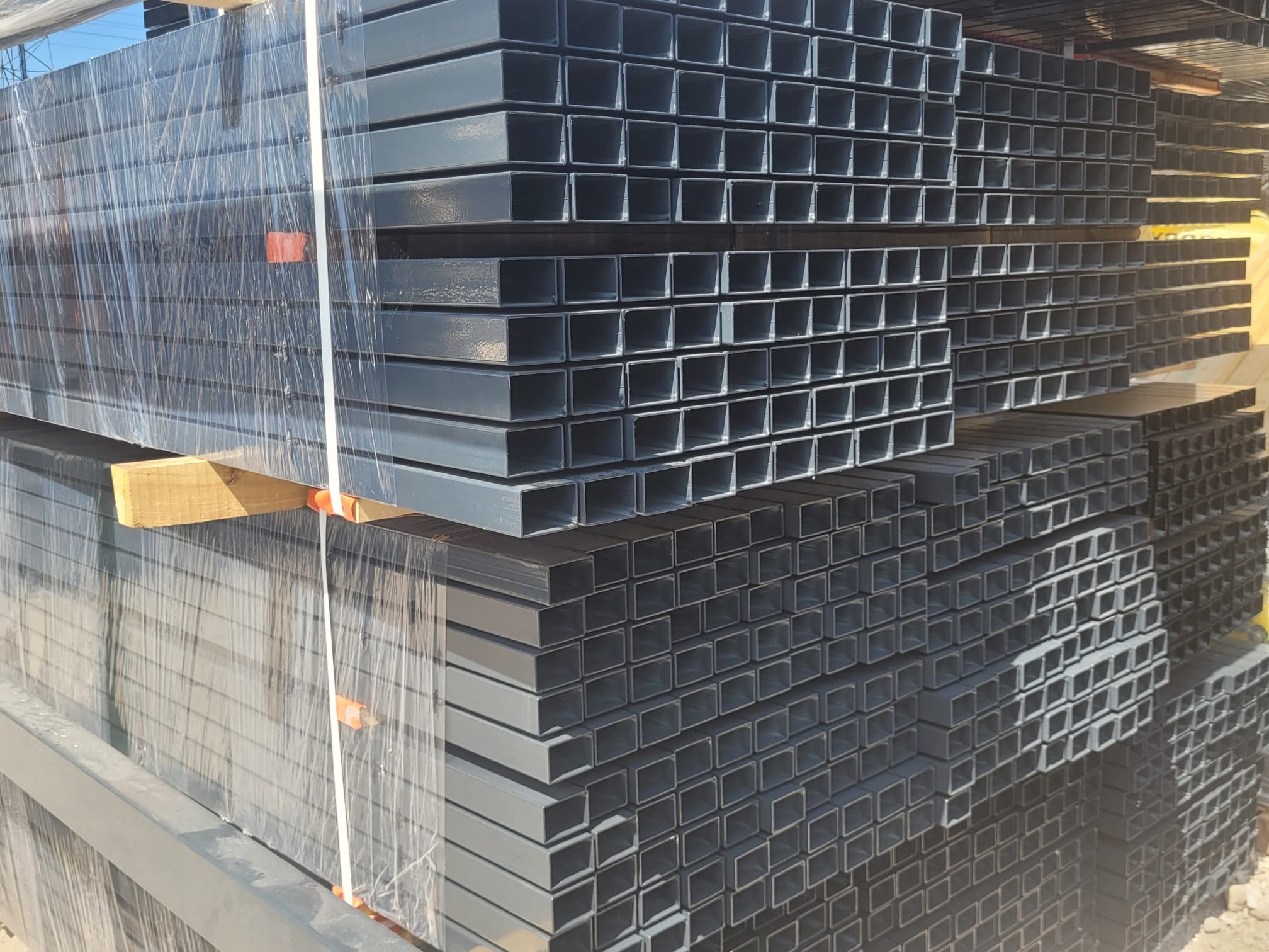 Stos ocynkowanych profili stalowych o przekroju kwadratowym, zabezpieczonych folią stretch na drewnianych legarach.