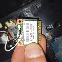 lublin.host KAROL RÓŻAŃSKI - Karta Wi-Fi Atheros AR5B225-REY M01 1229 Samsung, trzymana w palcach na tle wnętrza laptopa. Widoczne złącza i oznaczenia na karcie.