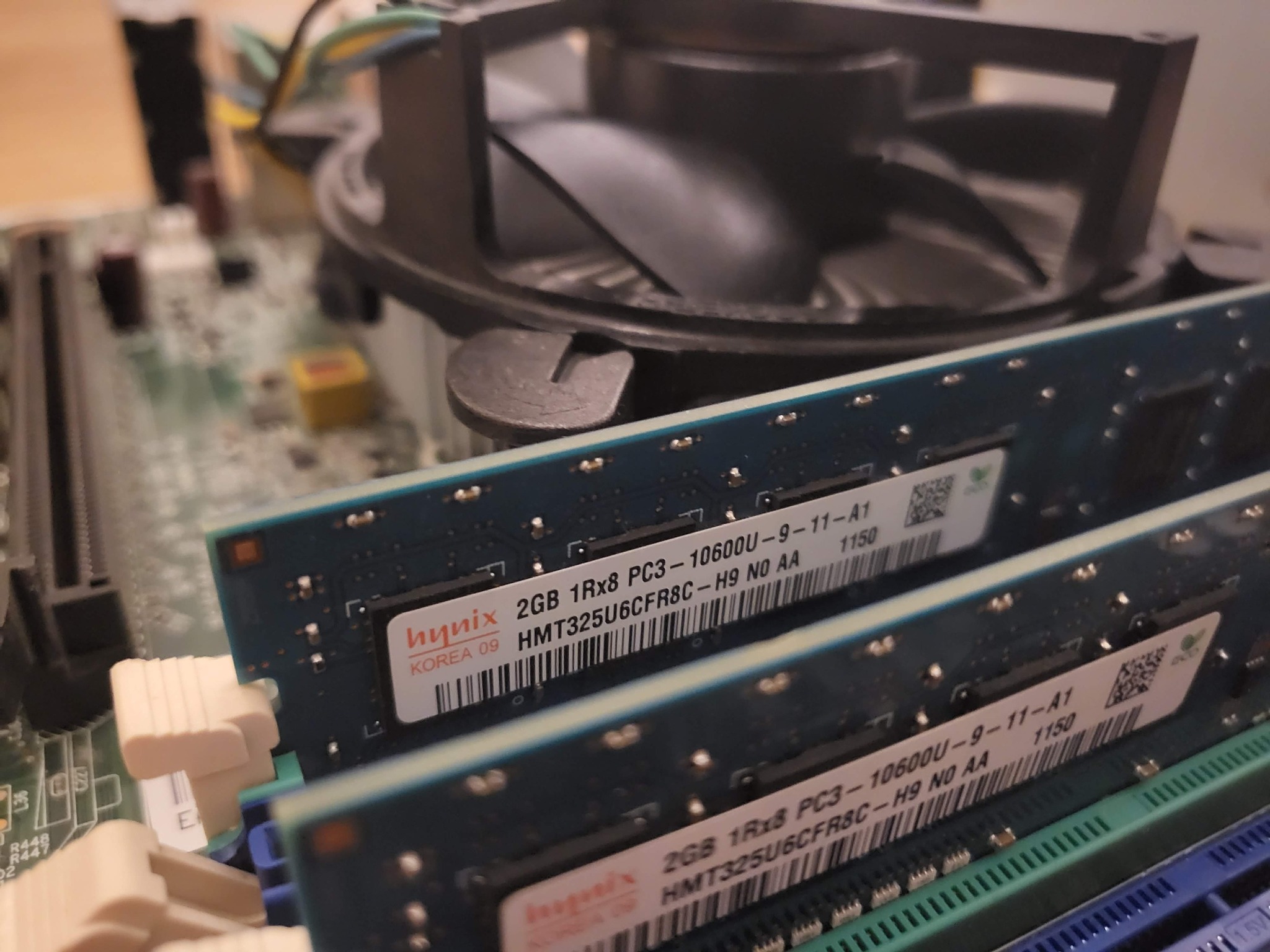 Wnętrze komputera stacjonarnego z bliska: dwa moduły pamięci RAM Hynix 2GB PC3-10600U, widoczne gniazda i radiator procesora. Detaliczna perspektywa.
