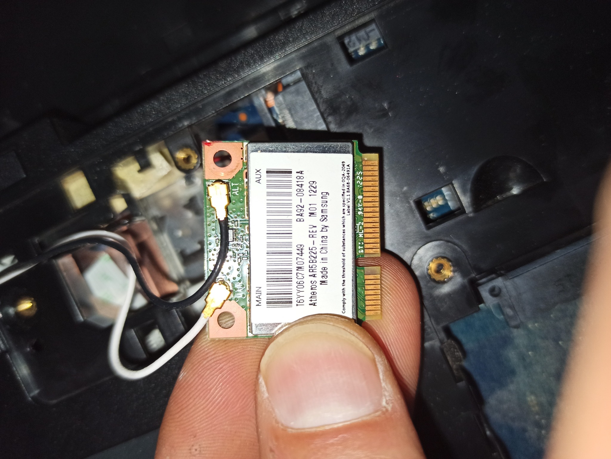 Karta Wi-Fi Atheros AR5B225-REY M01 1229 Samsung, trzymana w palcach na tle wnętrza laptopa. Widoczne złącza i oznaczenia na karcie.