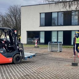 Centrum Szkoleniowe LDM w Legnicy - Grupa osób w kamizelkach odblaskowych obserwuje szkolenie z obsługi wózka widłowego Toyota Tonero 15 na placu manewrowym, w tle podnośnik koszowy i budynek.