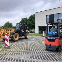 Centrum Szkoleniowe LDM w Legnicy - Żółta ładowarka teleskopowa JCB i pomarańczowy wózek widłowy Toyota na brukowanym placu, prawdopodobnie podczas szkolenia z obsługi maszyn budowlanych.