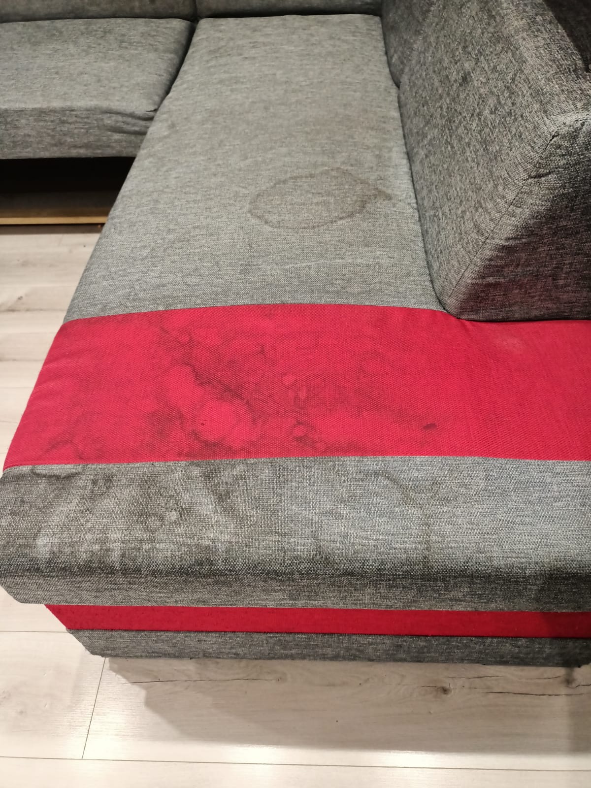 Szary narożnik z czerwonym pasem, widoczne plamy i zabrudzenia na tapicerce przed praniem.