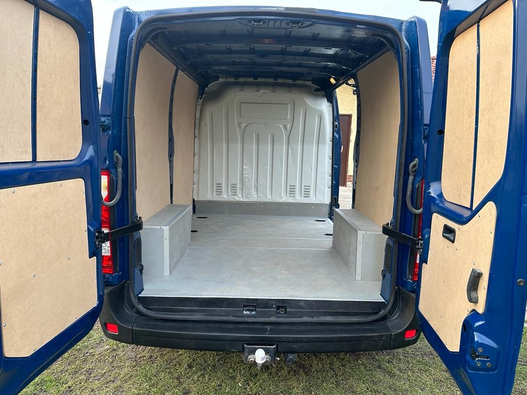 Wnętrze niebieskiego furgonu z otwartymi drzwiami, wyłożone płytami drewnianymi i wyposażone w szare, niskie szafki w przedniej części przestrzeni ładunkowej.