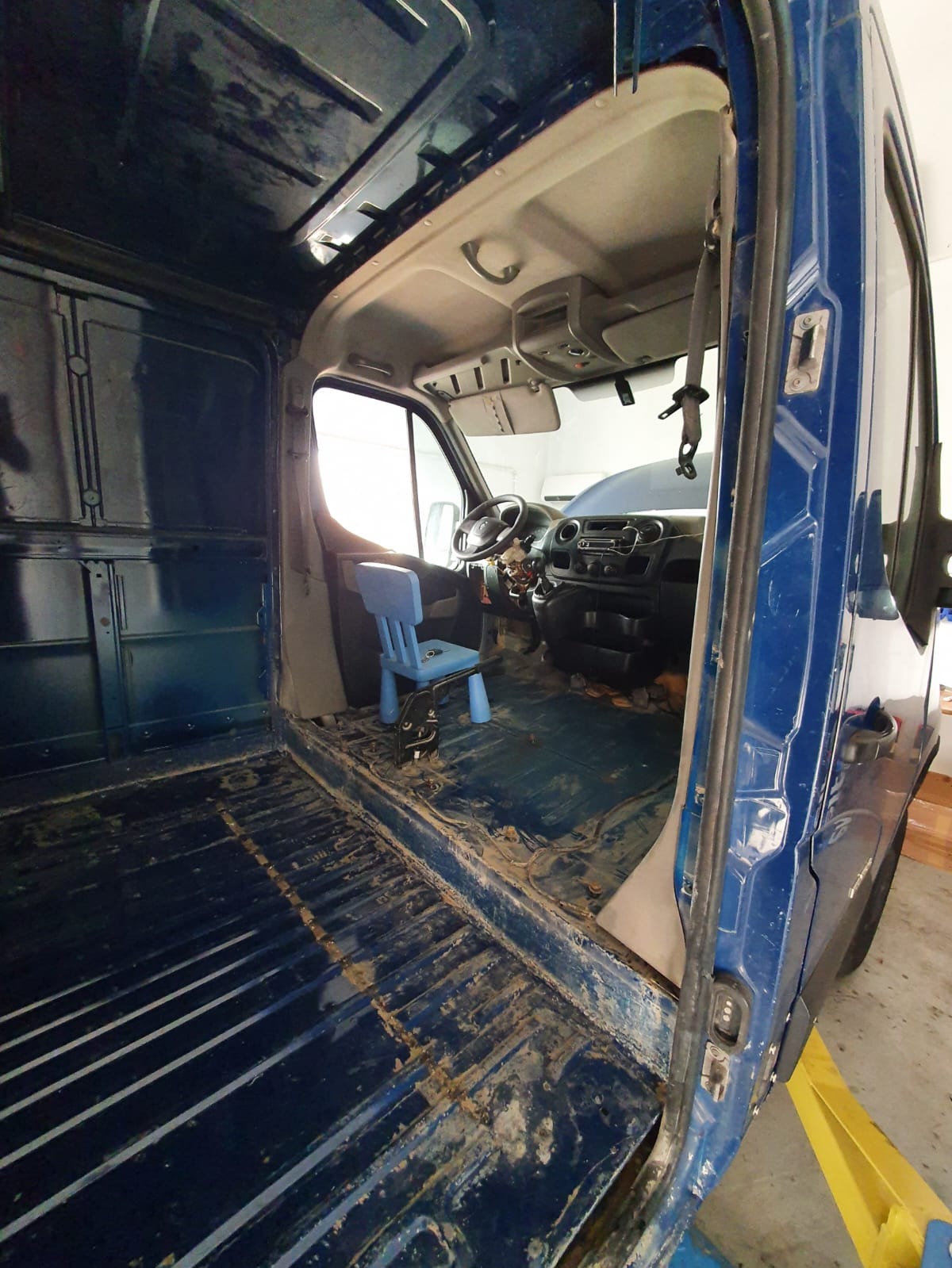 Wnętrze brudnego, niebieskiego furgonetki przed czyszczeniem, z małym niebieskim krzesłem dziecięcym w kabinie.