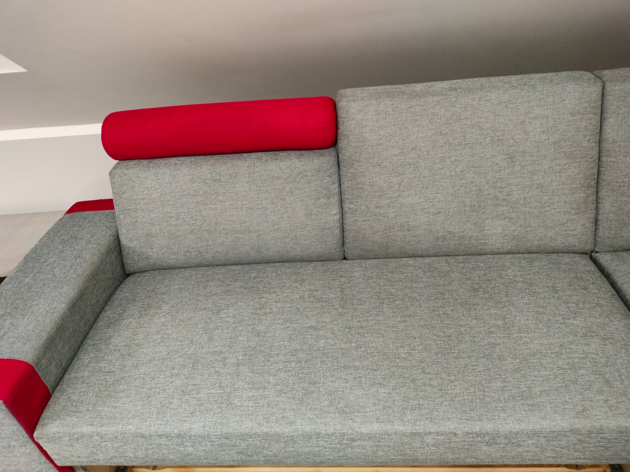 Szary narożnik z czerwonymi akcentami w postaci wałków i pasków na podłokietnikach, widok z góry na siedzisko i oparcie.