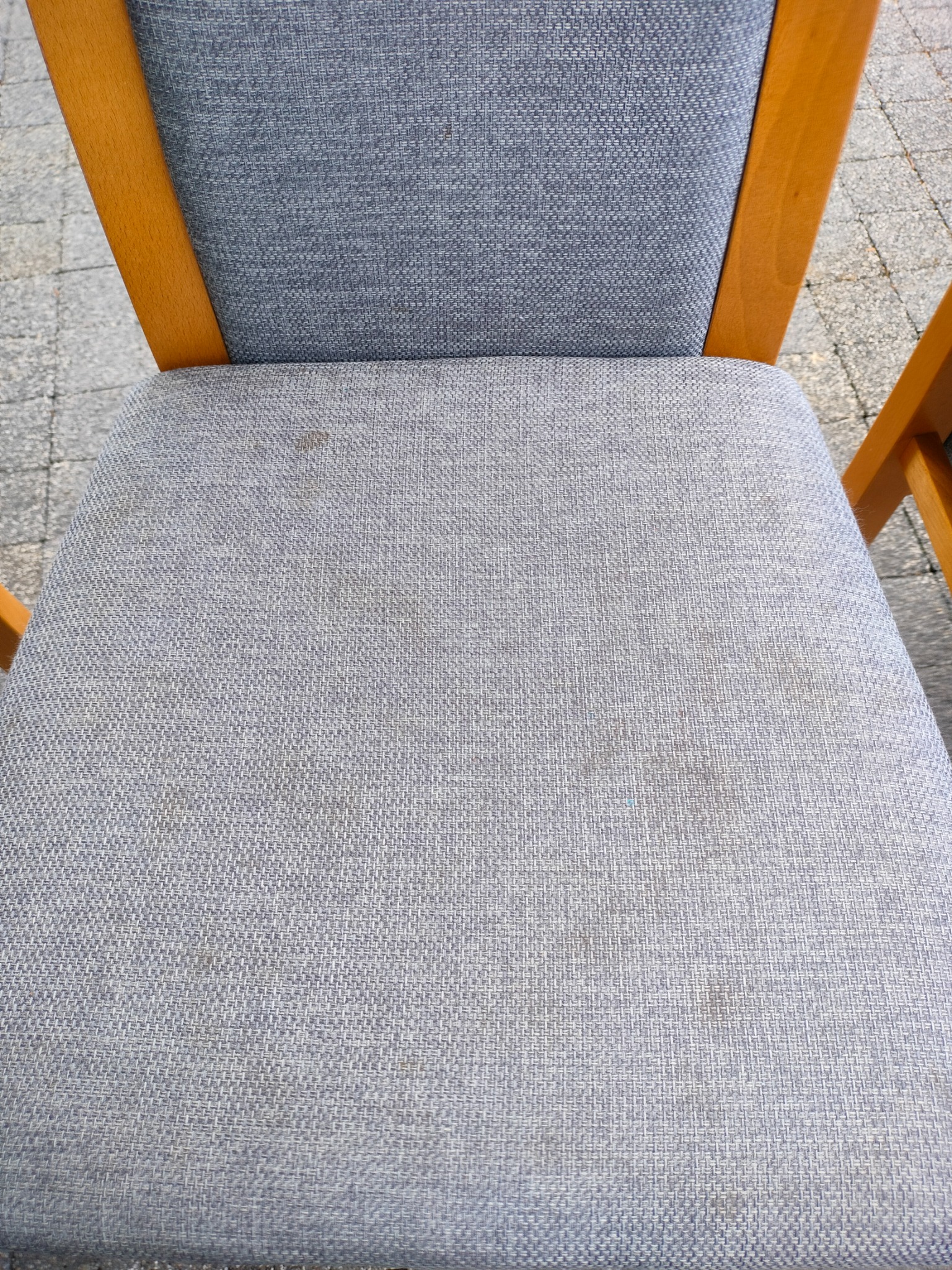 Bliski kadr na szare tapicerowane krzesło z drewnianą ramą, widoczne plamy na siedzisku, na zewnątrz.