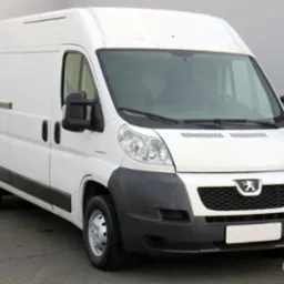 Biały Peugeot Boxer z wysokim dachem, widok z przodu na szarym tle, z widocznym logo producenta na grillu.