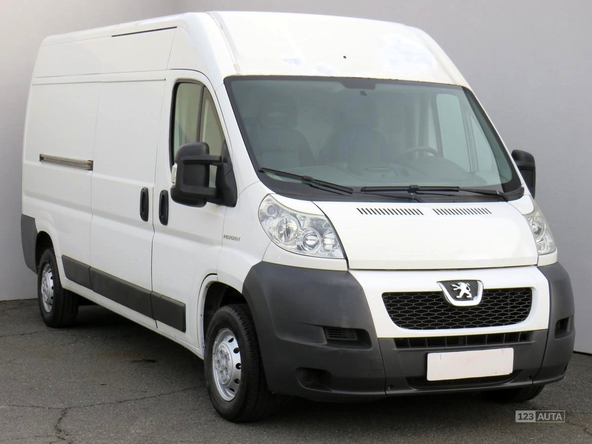 Biały Peugeot Boxer z wysokim dachem, widok z przodu na szarym tle, z widocznym logo producenta na grillu.