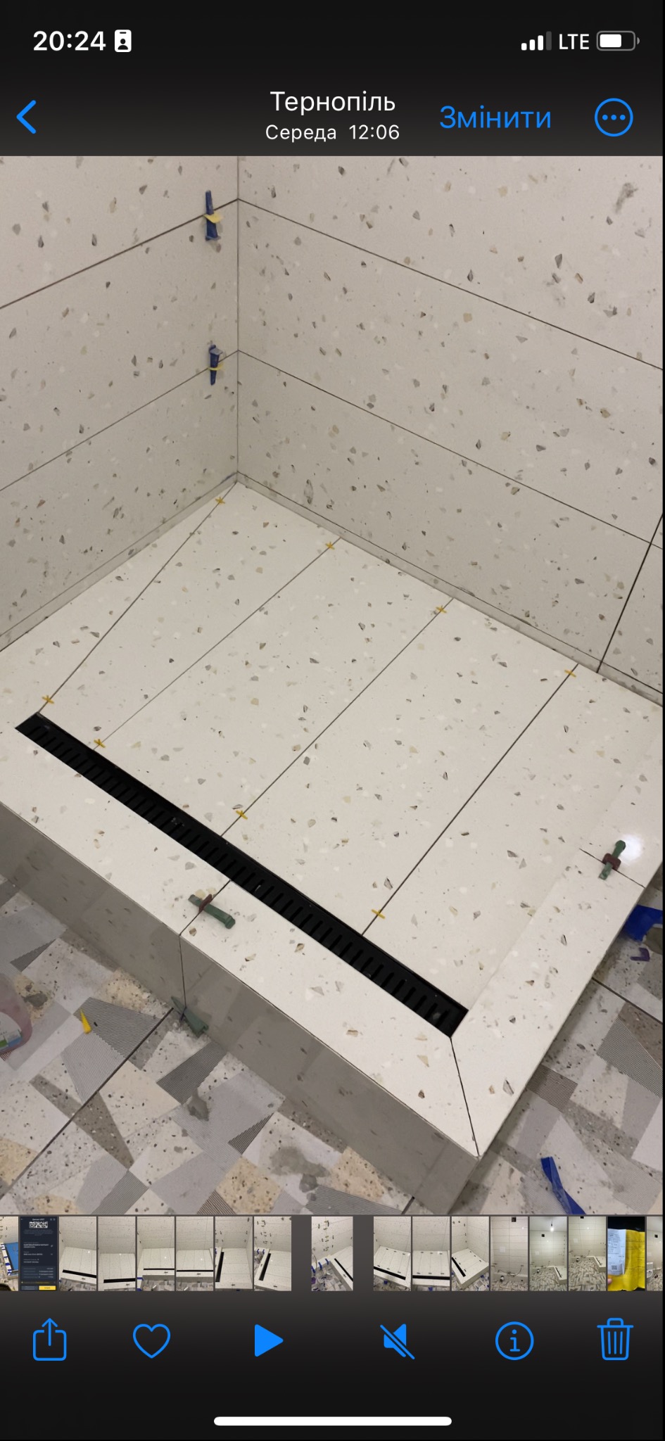 Białe płytki imitujące lastryko ułożone w kabinie prysznicowej z czarnym odpływem liniowym, widoczne krzyżyki dystansowe i klipsy poziomujące.