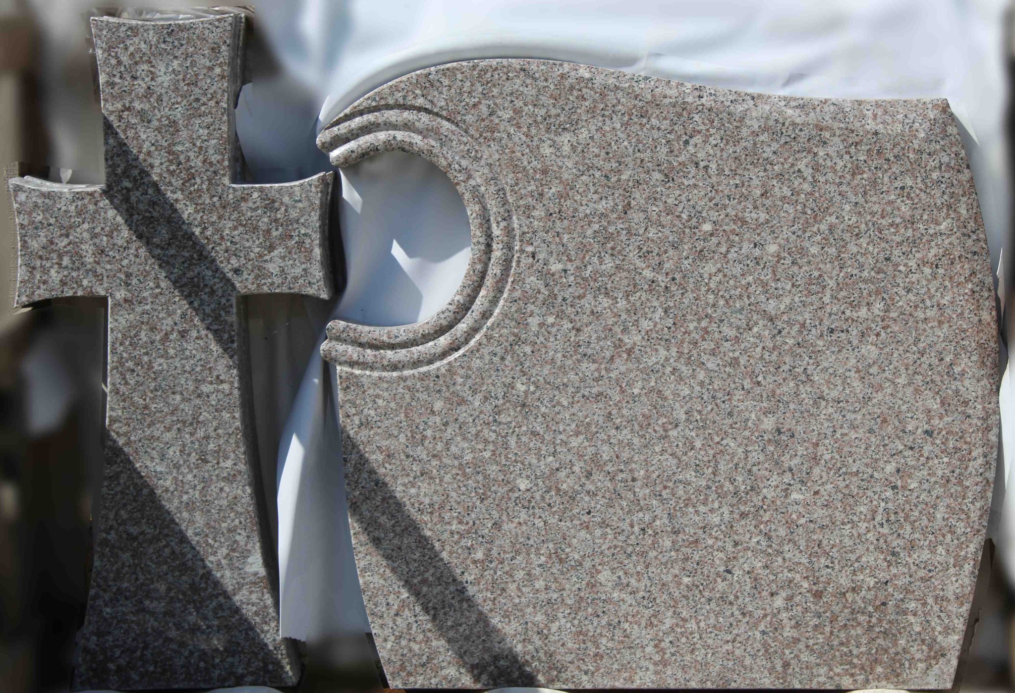 Surowe elementy nagrobka z różowego granitu: pionowy krzyż i tablica z wyciętym półkolem, przygotowane do montażu.