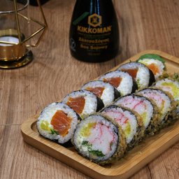 Sushimi Ursus - Różnorodny zestaw sushi na bambusowej tacy, z imbirem i butelką sosu sojowego Kikkoman w tle, obok dekoracyjnej świeczki w geometrycznym świeczniku.