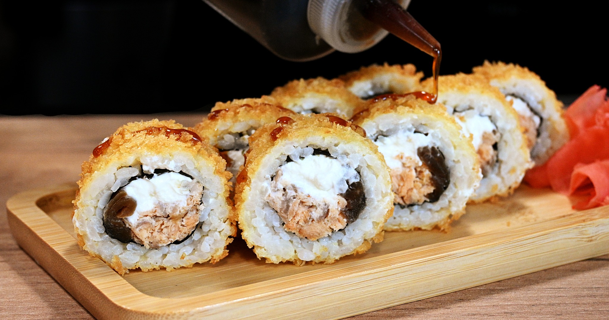 Smażone sushi z łososiem i kremowym serem, polane sosem sojowym na bambusowej desce, obok imbir