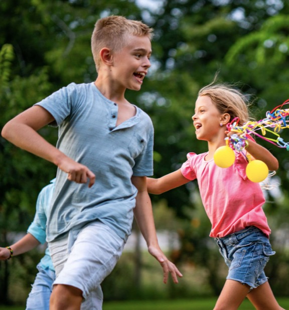 Radosne dzieci z kolorowymi rekwizytami podczas zabawy na urodzinach w Twardorzeczce, animator dla dzieci w akcji. Dziewczynka z uśmiechem goni chłopca.