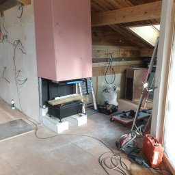 Blackwings - Wnętrze poddasza w trakcie montażu kominka z obudową z płyt gipsowo-kartonowych, widoczne narzędzia i materiały budowlane.