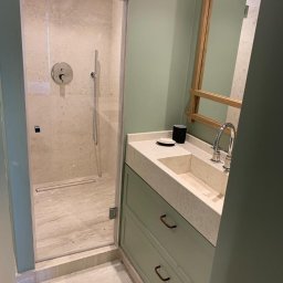 Blackwings - Nowoczesna łazienka z kabiną prysznicową ze szklanymi drzwiami, umywalką wpuszczaną w blat z szarego lastryko, szafką w kolorze pistacjowym z metalowymi uchwytami w kształcie litery C i dużym...