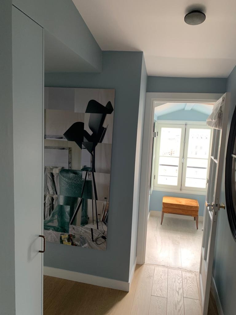 Wnętrze mieszkania w odcieniach błękitu z drewnianą podłogą, szafą w zabudowie, obrazem na ścianie i widokiem na pokój z pufą przy oknie.