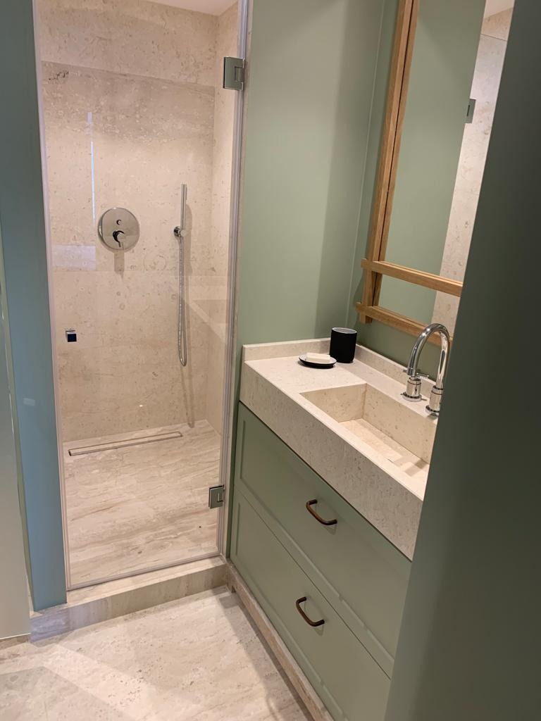 Nowoczesna łazienka z kabiną prysznicową ze szklanymi drzwiami, umywalką wpuszczaną w blat z szarego lastryko, szafką w kolorze pistacjowym z metalowymi uchwytami w kształcie litery C i dużym...