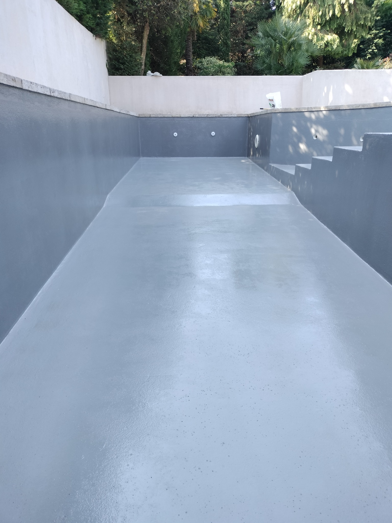 Pusty, wyremontowany basen z szarą, gładką powierzchnią ścian i dna, widoczne schody i otwory instalacyjne.
