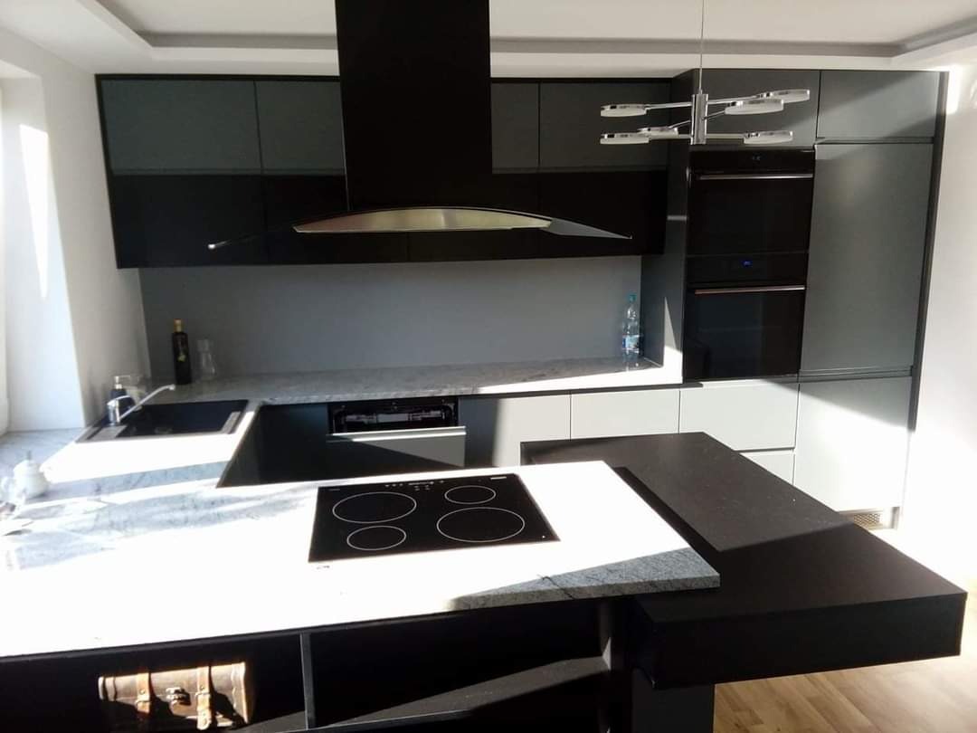 Nowoczesna kuchnia w odcieniach szarości i czerni z wyspą kuchenną o marmurowym blacie i czarną płytą indukcyjną, oświetlona przez designerską lampę sufitową.