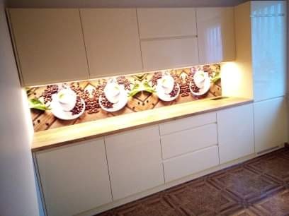 Jasna zabudowa kuchenna z drewnianym blatem i motywem filiżanek kawy na ścianie, widoczna z perspektywy pod kątem.