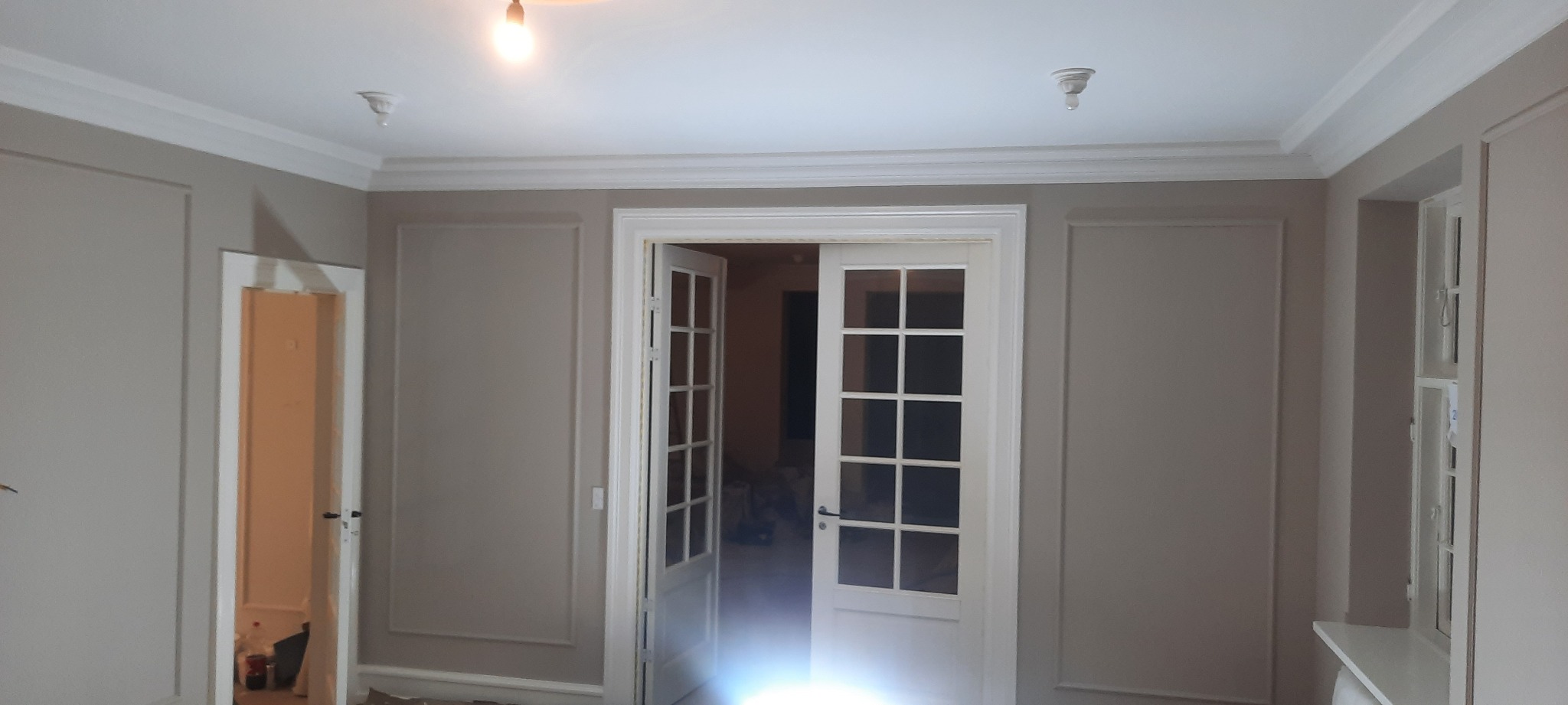 Pokój po remoncie z dekoracyjnymi panelami ściennymi w kolorze beżowym, białymi listwami przysufitowymi i białymi, przeszklonymi drzwiami wewnętrznymi.