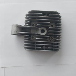 MARKING - Szara, żebrowana głowica silnika spalinowego, sfotografowana na białym tle pod lekkim kątem.