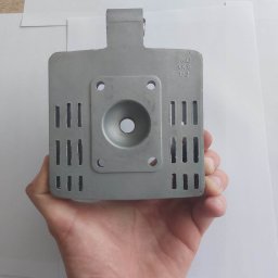 MARKING - Szary, metalowy element, prawdopodobnie głowica silnika, trzymany w dłoni na białym tle, widoczne otwory i napisy ZMD AK9 1/2.