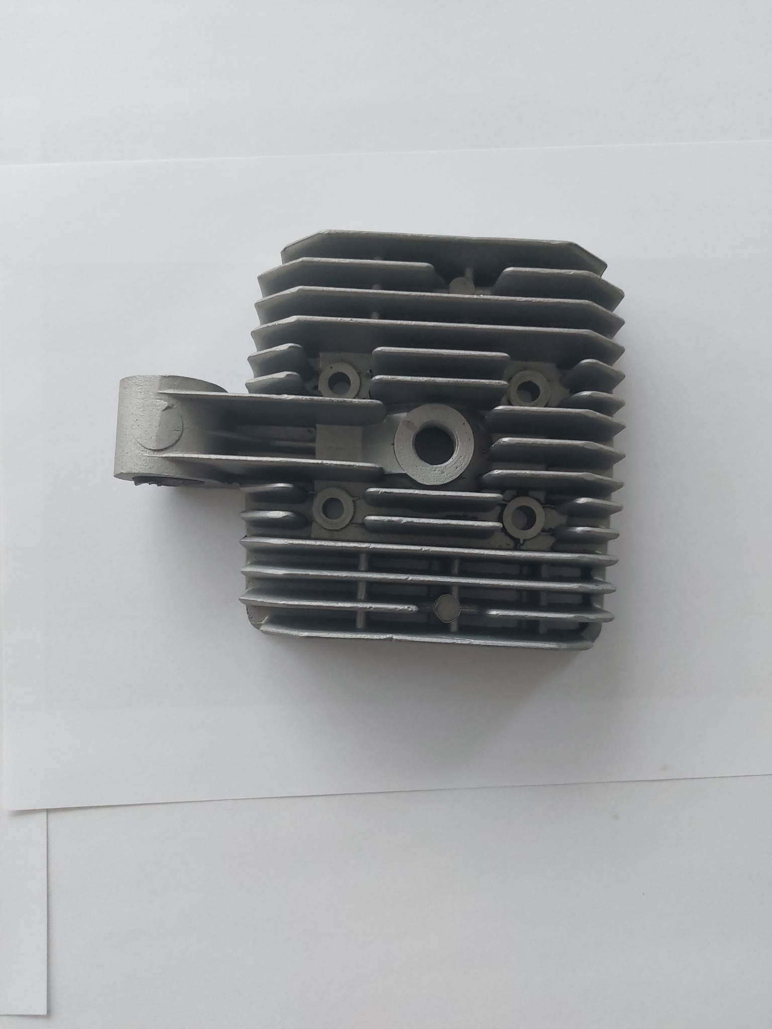 Szara, żebrowana głowica silnika spalinowego, sfotografowana na białym tle pod lekkim kątem.