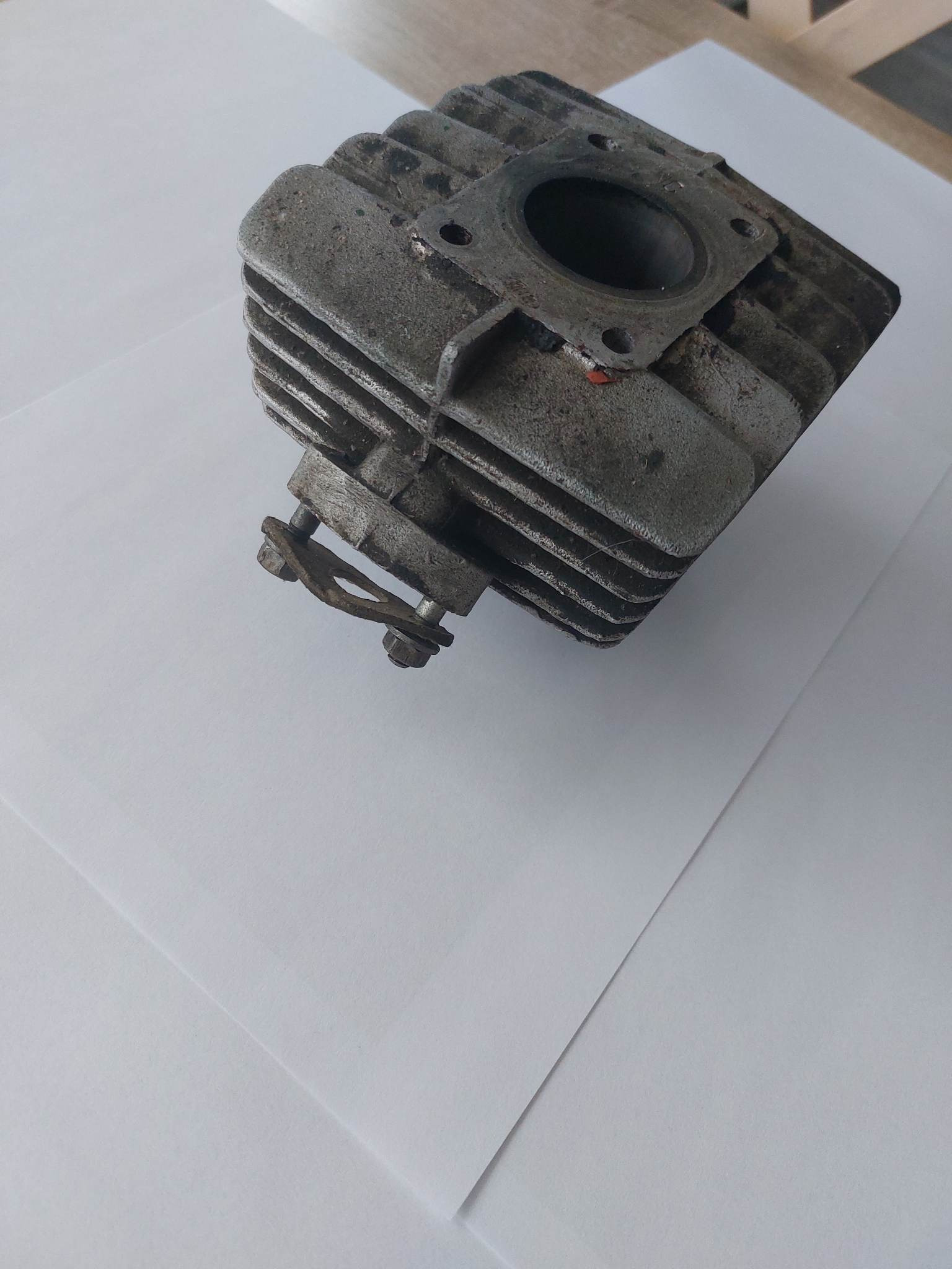 Cylindryczna głowica silnika spalinowego, widoczna na białym tle, z wyraźnymi śladami korozji i zabrudzeń, sugerująca potrzebę renowacji lub czyszczenia.