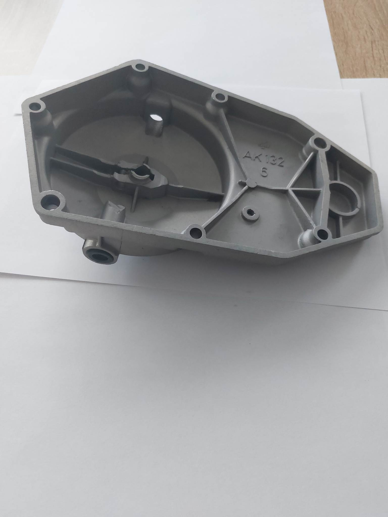 Szara, odlewana aluminiowa obudowa elementu mechanicznego z widocznymi otworami montażowymi i oznaczeniem AK132 6, leżąca na białym tle.