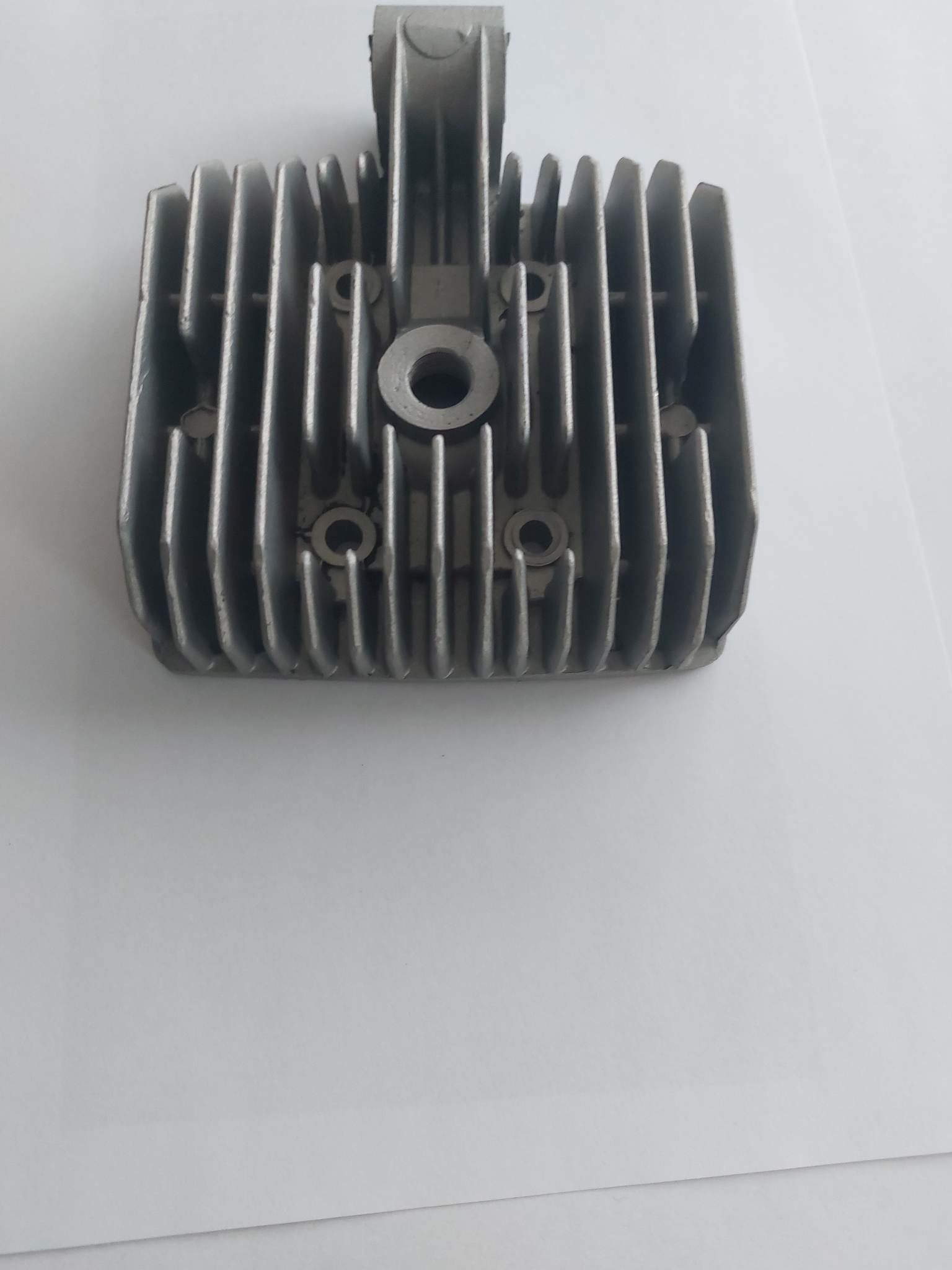 Szara, aluminiowa głowica silnika z żebrami chłodzącymi, widoczna od góry na białym tle.