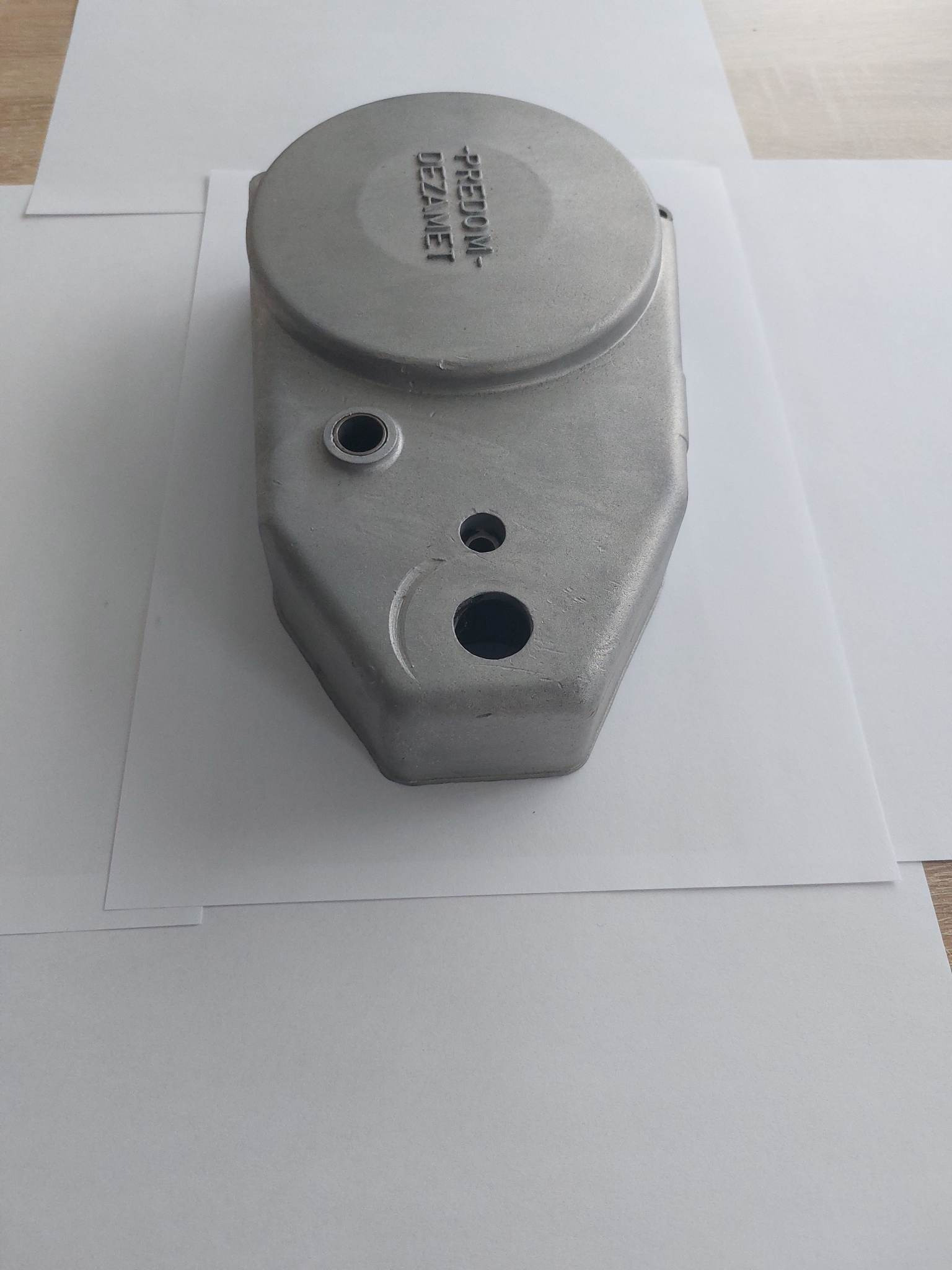 Szara, metalowa obudowa z trzema otworami i napisem 'FREDOM-DEZAMET' leżąca na białym papierze.