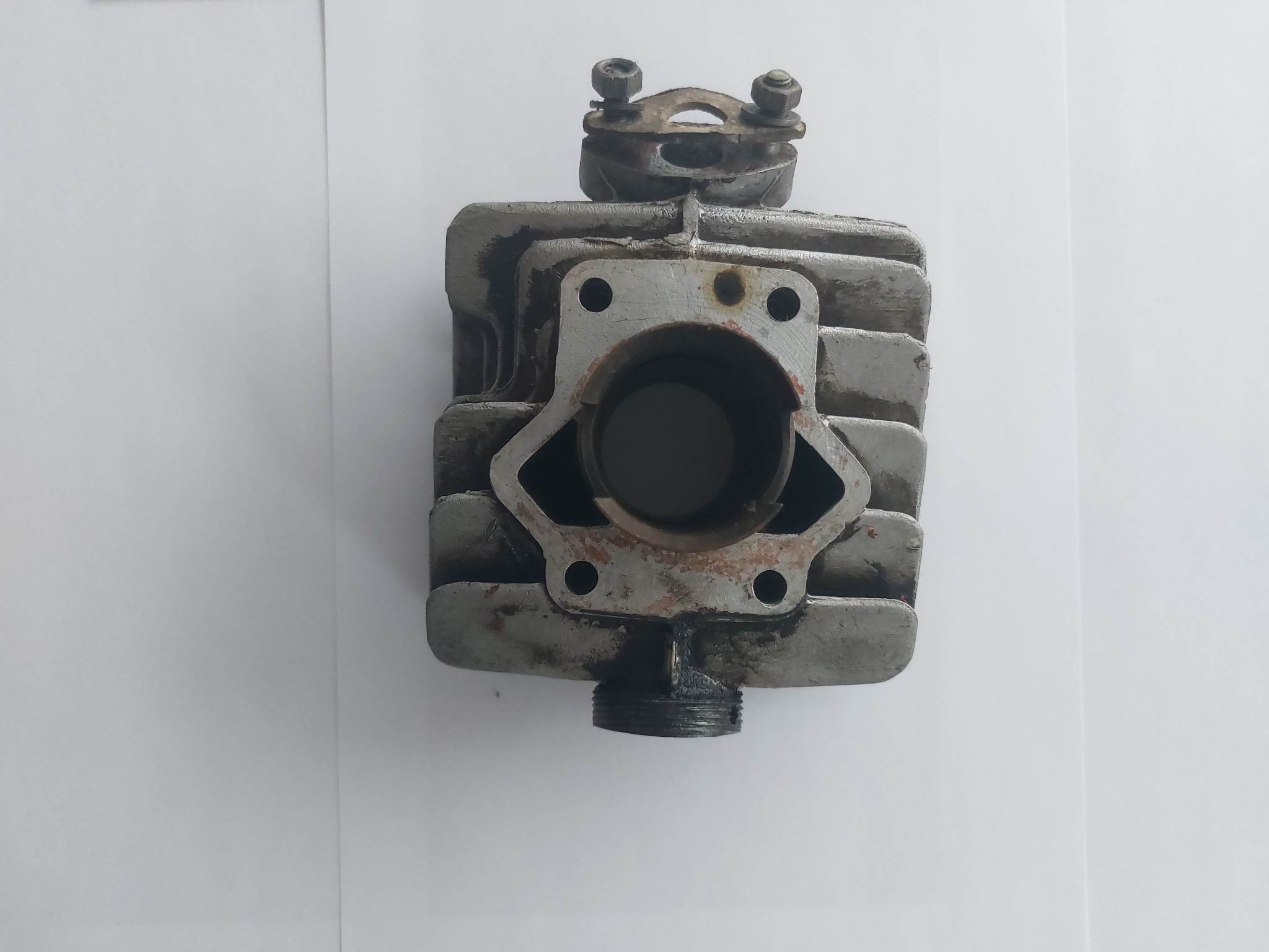 Cylindryczny blok silnika motocyklowego z widocznymi śladami korozji i gwintem u dołu, leżący na białym tle.