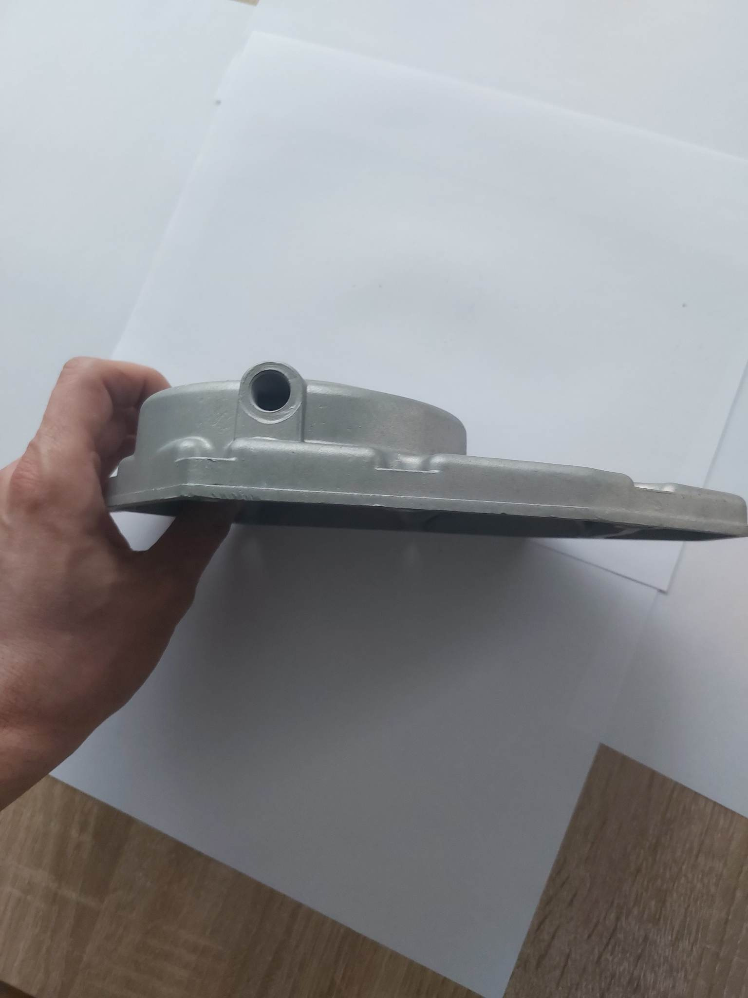 Szara, aluminiowa obudowa z otworem, trzymana w dłoni na tle białego papieru