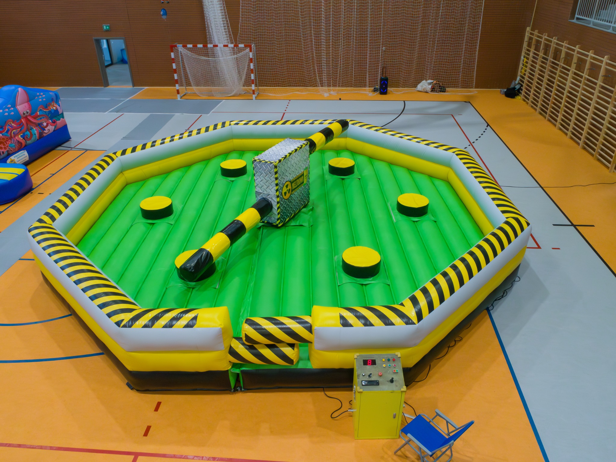 Atrakcja na wynajem w Lipnie: dmuchany tor przeszkód z motywem ostrzegawczym, ustawiony w hali sportowej. Żółto-czarne pasy, zielona podłoga, widoczny panel sterowania.