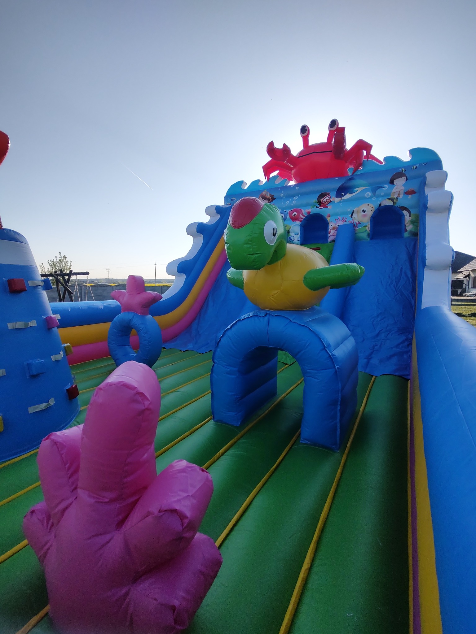 Kolorowy dmuchany plac zabaw z motywem morskim: krab, żółw, zjeżdżalnia i elementy wspinaczkowe. Idealny na imprezy plenerowe dla dzieci.