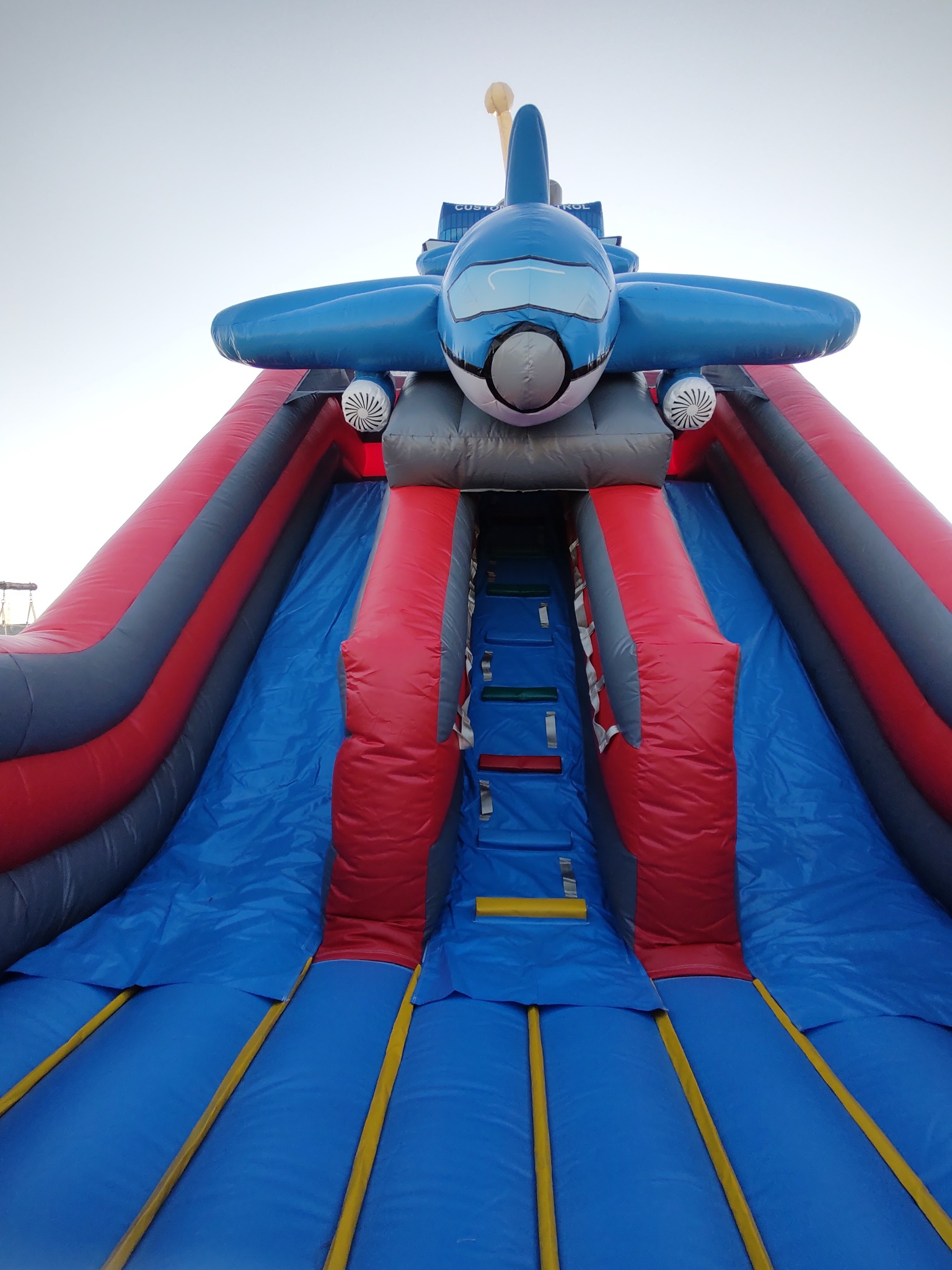 Kolorowa, dmuchana zjeżdżalnia w kształcie samolotu z drabinką i ślizgiem, idealna na imprezy plenerowe dla dzieci. Atrakcja z motywem lotniczym.