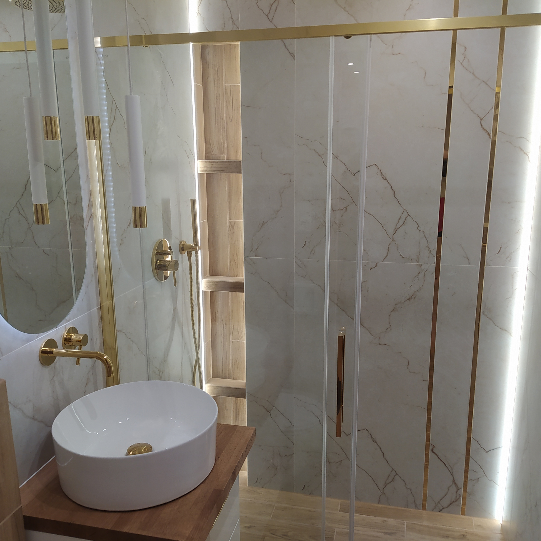 Elegancka aranżacja łazienki w Bełchatowie z umywalką nablatową, złotą armaturą i kabiną prysznicową z marmurowymi płytkami, uzupełniona o dekoracyjne oświetlenie LED.