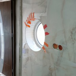 And-fliz - Okrągłe okno w ścianie wyłożonej płytkami imitującymi marmur, zabezpieczone taśmą malarską, widoczne gniazdka elektryczne, fragment ościeżnicy drzwi.