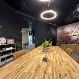 Nowoczesna sala konferencyjna z dużym drewnianym stołem, skórzanymi krzesłami, czarnymi ścianami i designerskim oświetleniem, z logo 'deal house' na ścianie w tle.