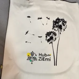 Biała torba bawełniana z nadrukowanymi dmuchawcami i logotypem 'Hub dla Ziemi' z kolorowymi akcentami.