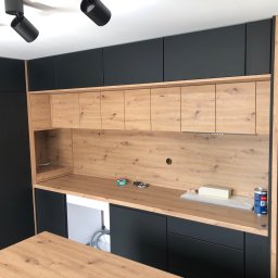 Meble na wymiar Damian Ratajczak - Nowoczesna kuchnia na wymiar z czarnymi szafkami górnymi i dolnymi oraz drewnianym blatem i szafkami wiszącymi, widoczne akcesoria montażowe na blacie.