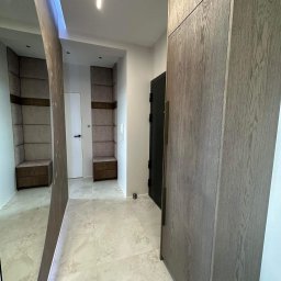 Meble na wymiar Damian Ratajczak - Nowoczesny przedpokój z dużą, drewnianą szafą, lustrem i wnękami z tapicerowanymi siedziskami, oświetlony ledowym światłem.