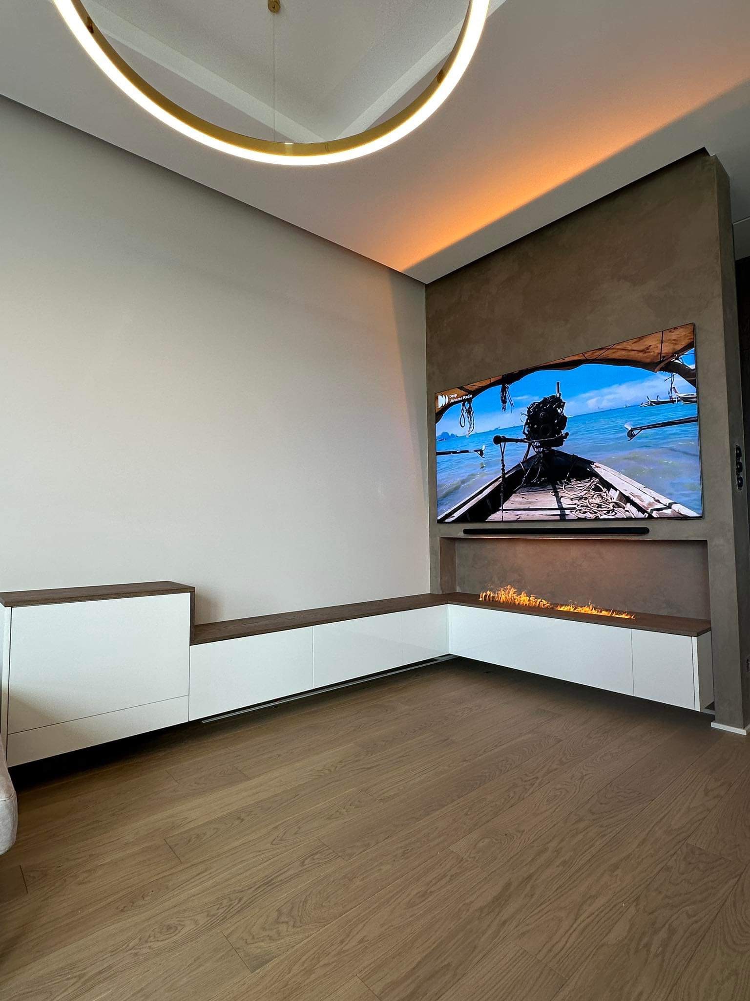 Nowoczesny salon z biało-drewnianą zabudową meblową, biokominkiem pod telewizorem i okrągłą lampą sufitową.