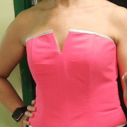 Len-iwa.shop - Kobieta pozuje w różowym gorsecie bez ramiączek z srebrnymi detalami, widoczny zegarek na nadgarstku i fragment zielonych drzwi w tle.